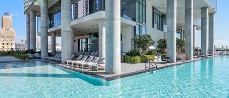 Ein modernes Gebäude mit Pool auf dem Dach, großen Säulen und Blick auf die Skyline der Stadt.
