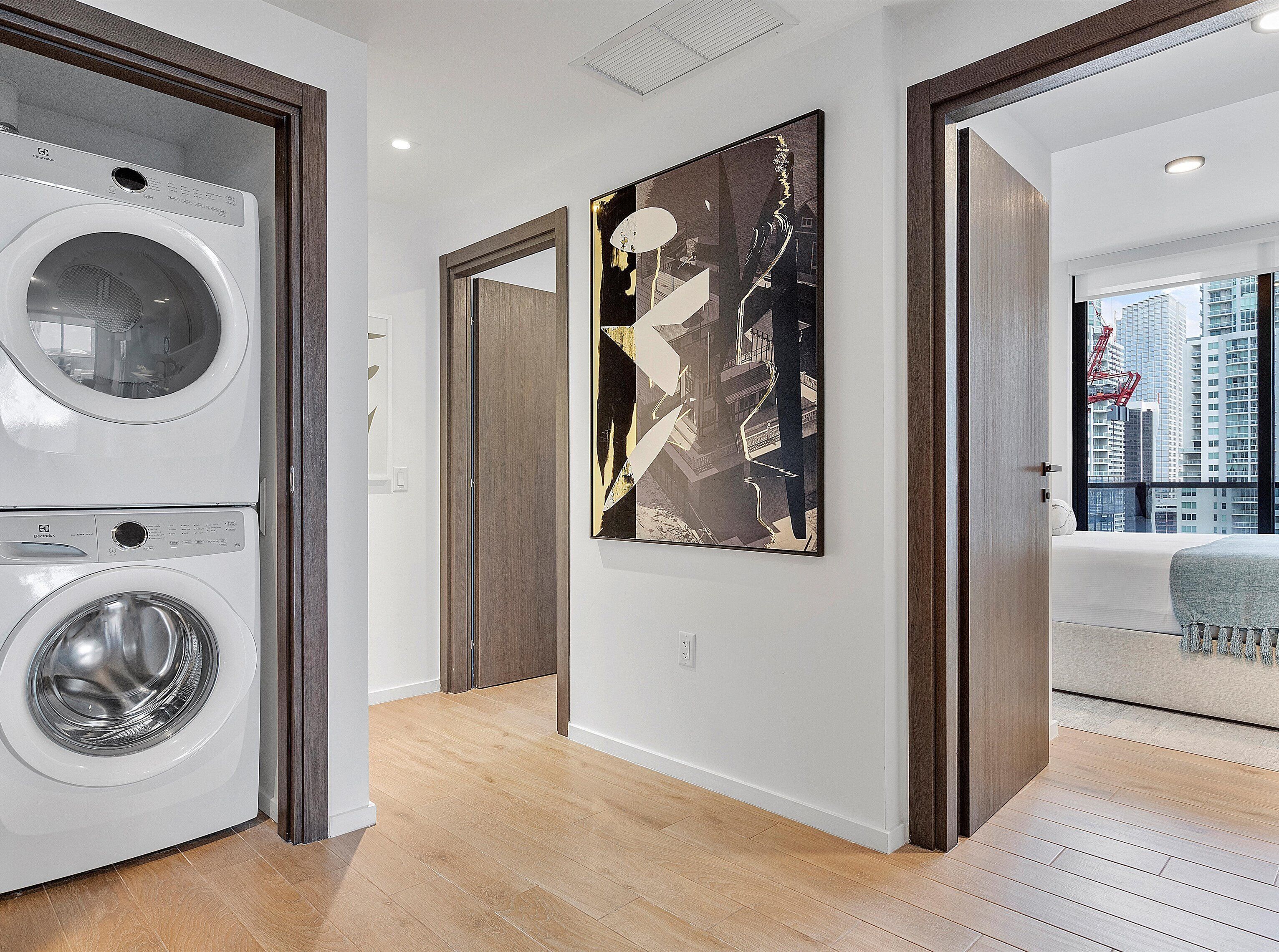 Un apartamento moderno con lavandería, un cuadro abstracto grande y vistas de la ciudad a través de una ventana.