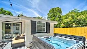 Un bain à remous sur une terrasse en bois, avec un espace patio fermé par des baies vitrées et des meubles d’extérieur.