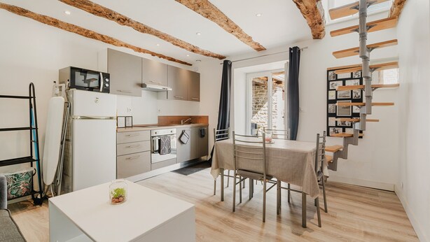 Een moderne keuken met houten balken, een eethoek met tafel en stoelen, en een trap met een inbouwplank.