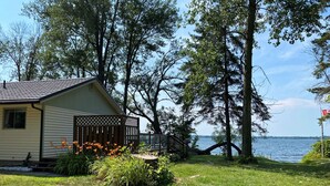 Eine Hütte mit einer Terrasse mit Blick auf einen See, umgeben von Bäumen und einer Wiese.