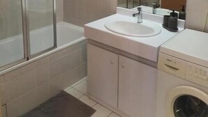 Un bagno con doccia, lavandino, specchio e lavatrice.