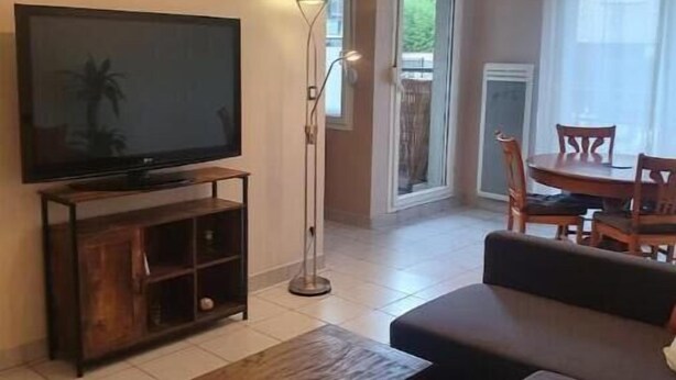 Un soggiorno con una TV a schermo piatto su un supporto in legno, una lampada da terra, un divano e un'area pranzo con tavolo e sedie.