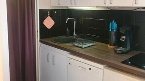 Una cucina compatta con mobili bianchi, un lavello in acciaio inossidabile, una macchina da caffè e un espositore per piatti.