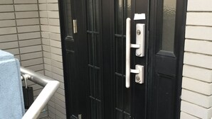 Una puerta negra con pomo y cerradura, una barandilla de metal y un suelo de baldosas.