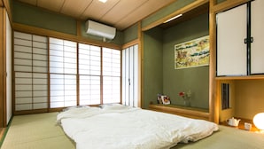 Una habitación japonesa tradicional con suelo de tatami, una cama grande, puertas correderas shoji y un estante pequeño con libros y un jarrón.