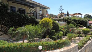 A landscaped garden with a stone wall, various plants, and a building with a tiled roof. - 4 Bedrooms, perfect sea views, Infinity pool, Hot tub, Walk to beach & tavernas. (Chania)