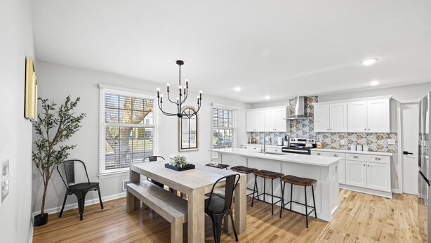 Una cocina moderna con armarios blancos, una mesa de comedor de madera y una lámpara de araña.