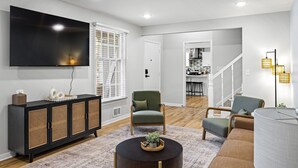 Una sala de estar moderna con un televisor de pantalla plana, un mueble negro, un sillón verde, un sofá marrón y una mesa de centro redonda.