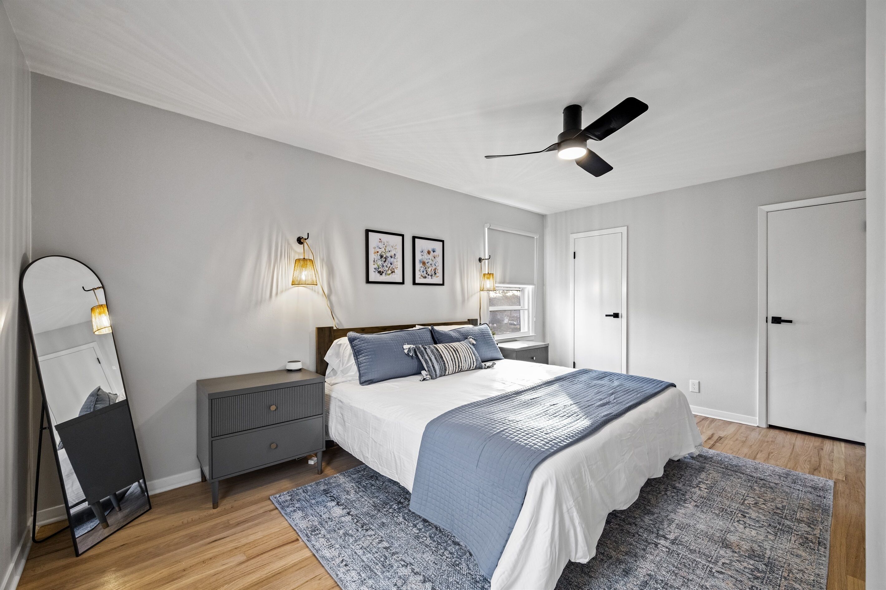 Een slaapkamer met een bed, nachtkastjes, een spiegel en een plafondventilator.