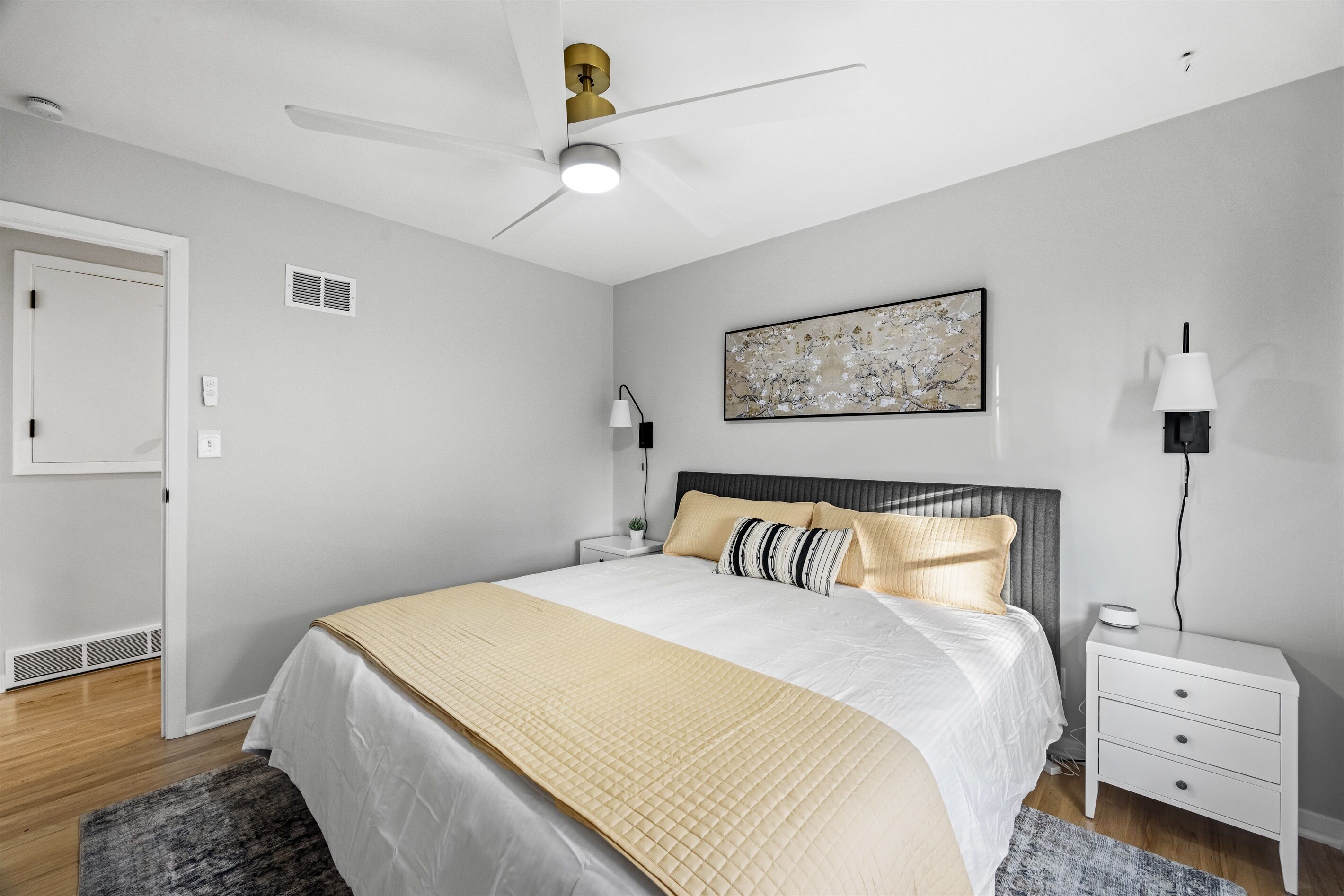 A neatly arranged bedroom with a bed, bedside tables, a ceiling fan, and a wall-mounted artwork.