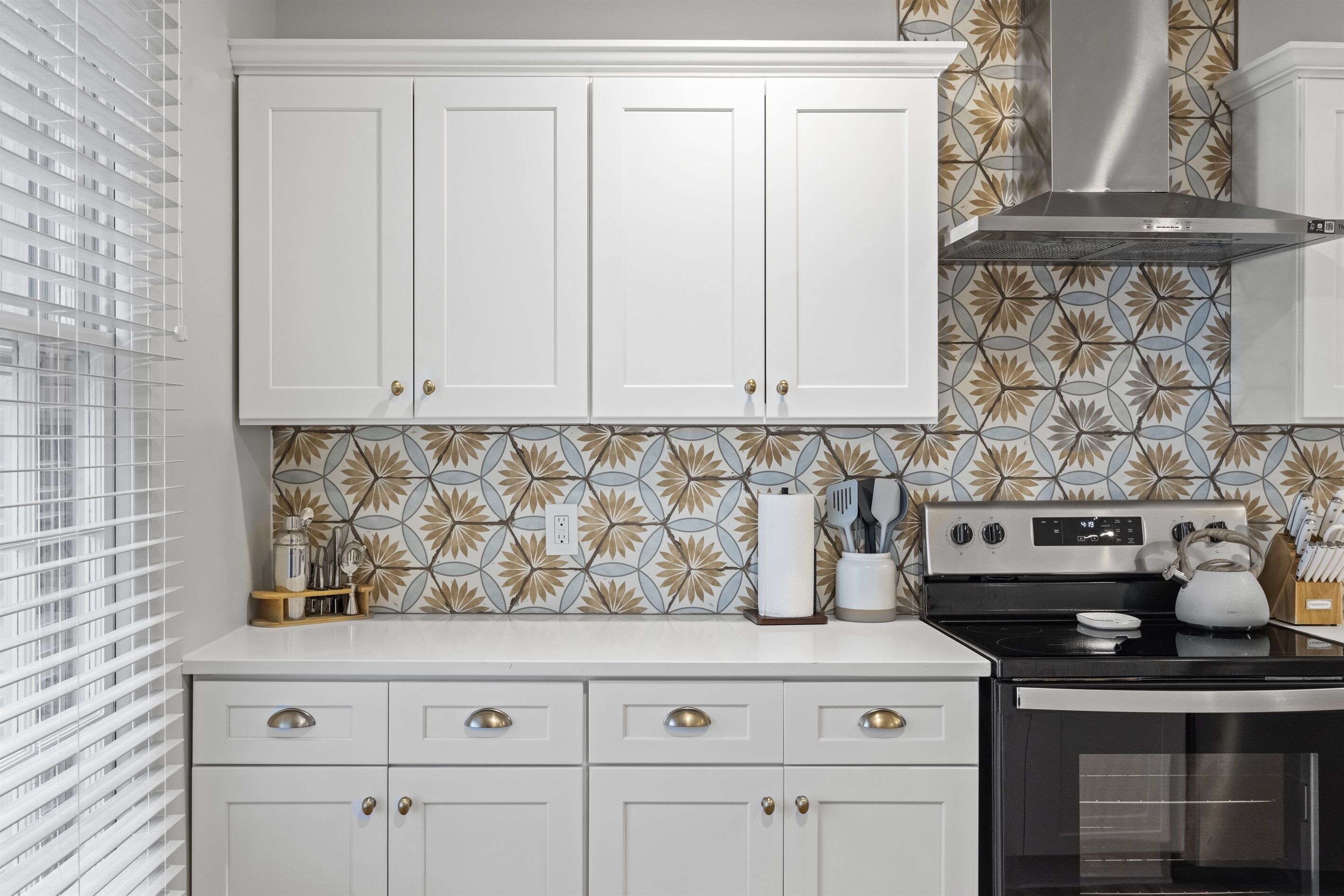 A kitchen with white cabinets, a stainless steel range hood, and a patterned backsplash.