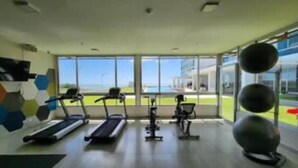 Un gimnasio con cintas de correr, bicicletas estáticas y pelotas de ejercicio, ventanas amplias y vistas al exterior.