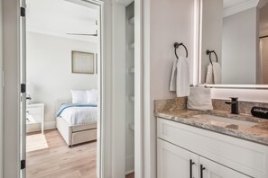 Habitación de hotel con cama, baño con lavamanos y espejo, y una puerta que da a otra habitación.