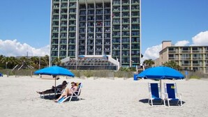Ein Hotel mit mehreren Etagen und Balkonen, Strandliegen und Sonnenschirmen.