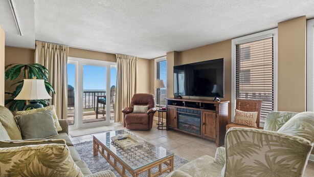 A living room with a sofa, armchairs, a coffee table, a TV, and a fireplace. - Sea Marsh I 104 - 3BD/2.5BA - Oceanfront (North Myrtle Beach)