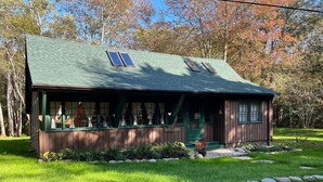 A rustic cabin with a green roof, two windows with shutters, and a porch with a sign reading "Stillmeadow". - Charming, quiet 3-BR cottage; private access to cove and forest trails (Phippsburg)
