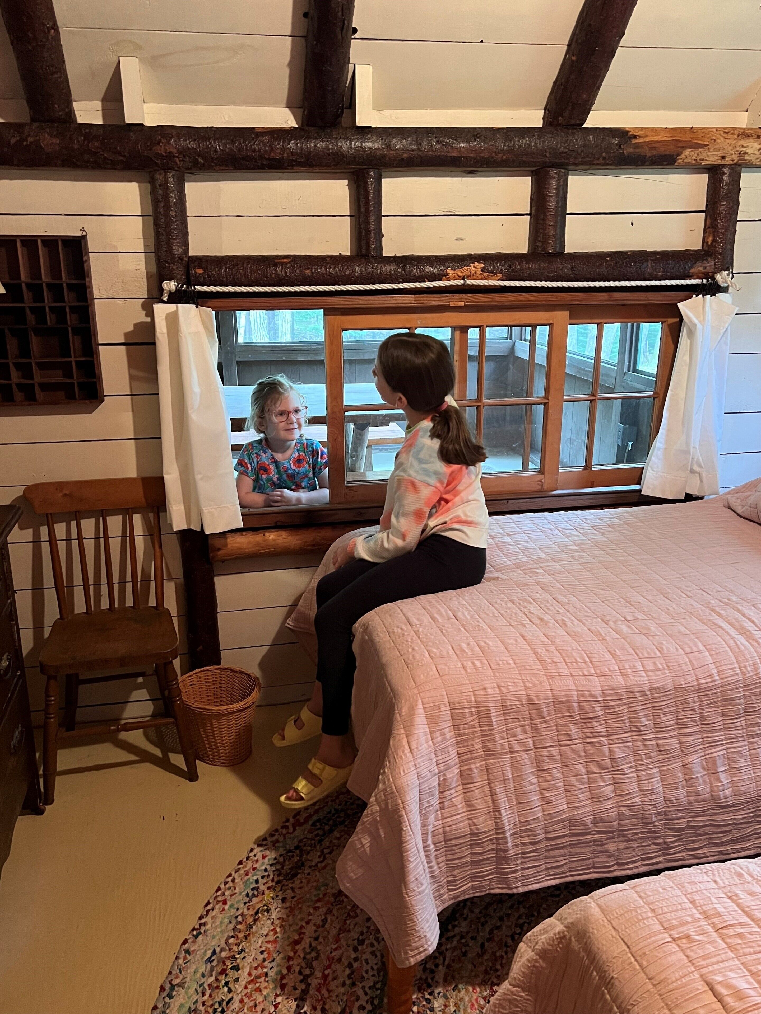 A cozy room with a bed, a window with curtains, a wooden chair, and a wicker basket.