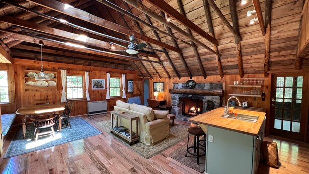 A spacious log cabin interior with a high ceiling, a fireplace, a dining area, and a kitchen with a bar. - Charming, quiet 3-BR cottage; private access to cove and forest trails (Phippsburg)