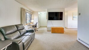 Un salon avec un canapé en cuir, un banc en bois, un téléviseur à écran plat et une petite table avec une lampe.