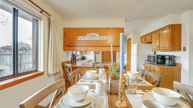 Un coin repas avec une table en bois dressée pour le repas, une cuisine en arrière-plan et un panneau indiquant : « Repas faits maison ».