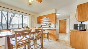 Une cuisine moderne avec des meubles en bois, un coin repas comprenant une table et des chaises en bois, et une grande fenêtre donnant sur la forêt.