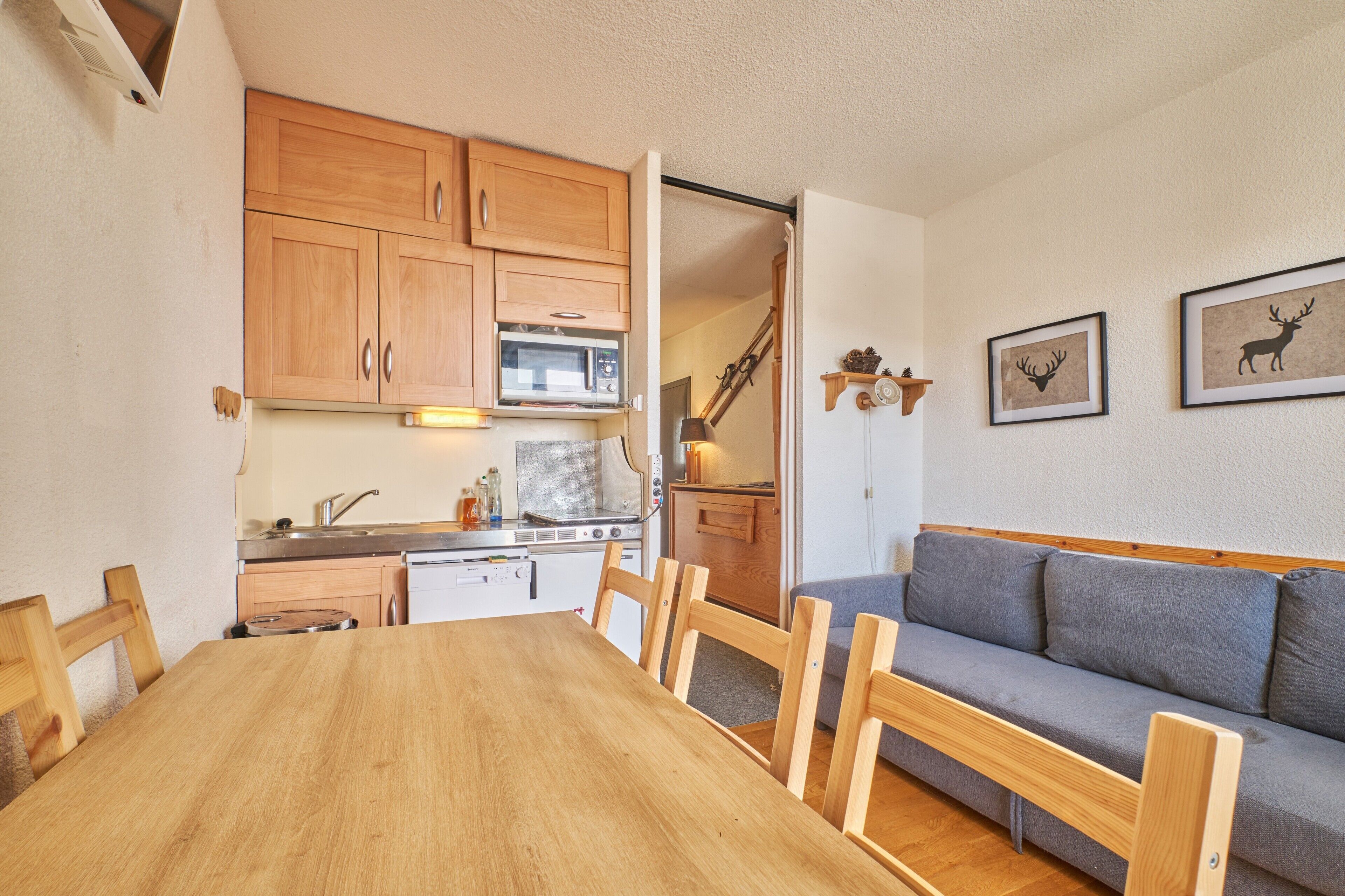Une cuisine compacte avec des meubles en bois, un four à micro-ondes et une cuisinière. On y trouve une table à manger avec des chaises et un canapé gris.