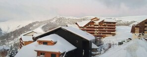 Un pueblo nevado en la montaña con varios edificios, incluyendo un hotel grande con balcones y un edificio más pequeño en primer plano.