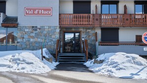L’entrée d’un hôtel avec une façade en pierre, des balcons en bois et une enseigne indiquant « Val d’Huez ».