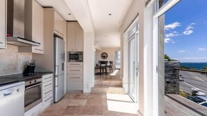 Una cocina moderna con electrodomésticos de acero inoxidable, un comedor con una mesa redonda y vistas al mar a través de amplios ventanales correderas.