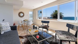 Una sala moderna con un amplio ventanal con vistas al mar, un comedor con mesa y sillas, y una zona de estar acogedora con sofá y sillones.