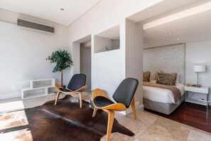 Ein modernes Hotelzimmer mit einem großen Bett, zwei Sesseln, einer kleinen Pflanze und einem weißen Konsolentisch.