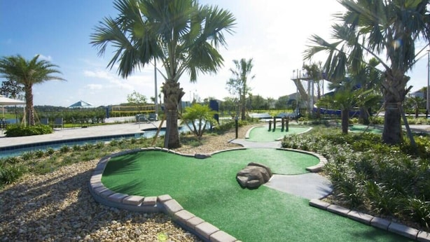 Un parcours de minigolf avec un espace de putting verdoyant, des palmiers et une piscine en arrière-plan.