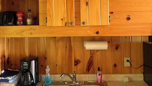 A kitchen with wooden cabinets, a stainless steel sink, a coffee maker, and a roll of paper towels. - Ruth Lake Resort Cabin # 4 (Spurr Township)
