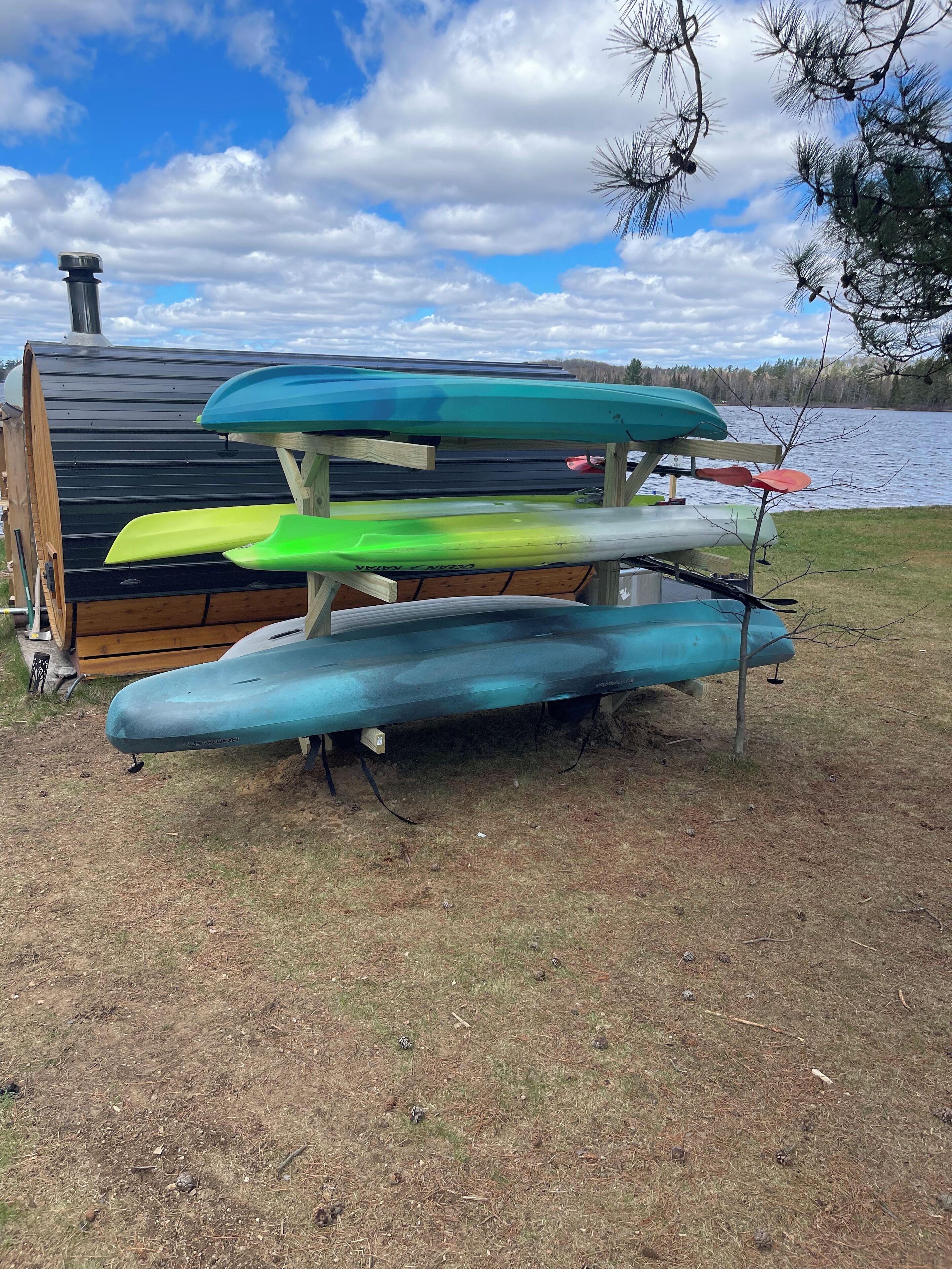 Una hilera de kayaks sobre un soporte de madera cerca de un lago, con un edificio al fondo.