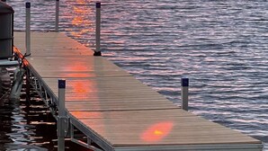 Une jetée en bois s’étendant sur une étendue d’eau calme, avec un coucher de soleil en arrière-plan.