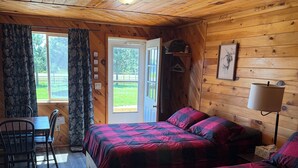 A cabin with two beds, a dining table, chairs, a lamp, and a window with curtains. - Ruth Lake Resort Cabin #2 (Spurr Township)