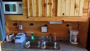 A compact kitchen with wooden cabinets, a microwave, a toaster, a coffee maker, and a sink. - Ruth Lake Resort Cabin #2 (Spurr Township)