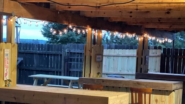 Une structure extérieure en bois comprenant un espace bar, avec un comptoir et des tabourets.