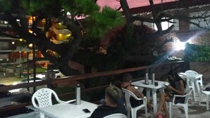 Un espacio al aire libre con mesas y sillas, un árbol y un edificio de fondo.