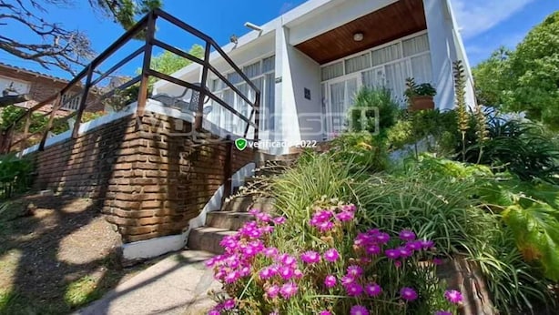 Una casa moderna con una escalera de ladrillo, una terraza de madera y un jardín con flores rosas.