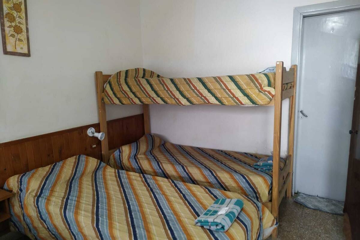 Una cama litera con ropa de cama a rayas en una habitación con una puerta de madera y un cuadro en la pared.