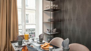 Desayuno con croissants, jugo de naranja y tazas de café sobre una mesa con vistas a la ciudad a través de amplios ventanales.