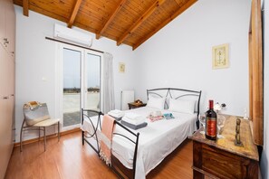 A bedroom with a bed, a chair, a bedside table, a wooden dresser, and a window with a view.