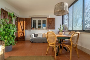 A dining area with a table and chairs, a hanging light fixture, and a large window with a view.