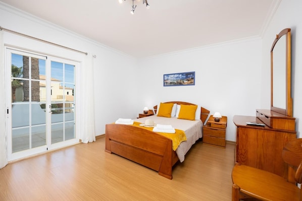 Ein Schlafzimmer mit einem hölzernen Bett, einem Schreibtisch, einem Stuhl und einem großen Fenster mit Blick auf Gebäude.