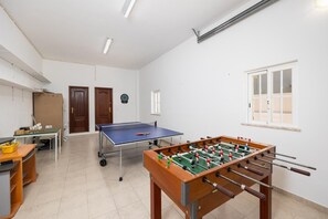 Ein Zimmer mit Tischtennisplatte, Kicker, Schreibtisch mit Stuhl und Fenster.
