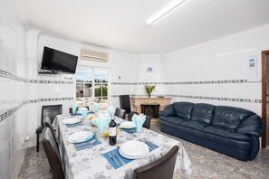 Ein Essbereich mit einem Tisch für vier Personen, einem schwarzen Ledersofa, einem Kamin und einem an der Wand befestigten Fernseher.