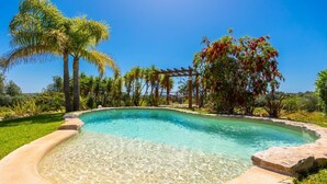 Une piscine aux eaux cristallines, agrémentée d’une pergola en bois et bordée de palmiers.