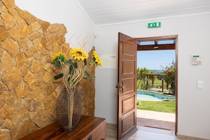 Eine Steinsäule, eine Holztür und Blick auf einen Pool und Garten.
